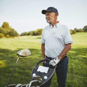 Senior man standing with his golf clubs on a fairway